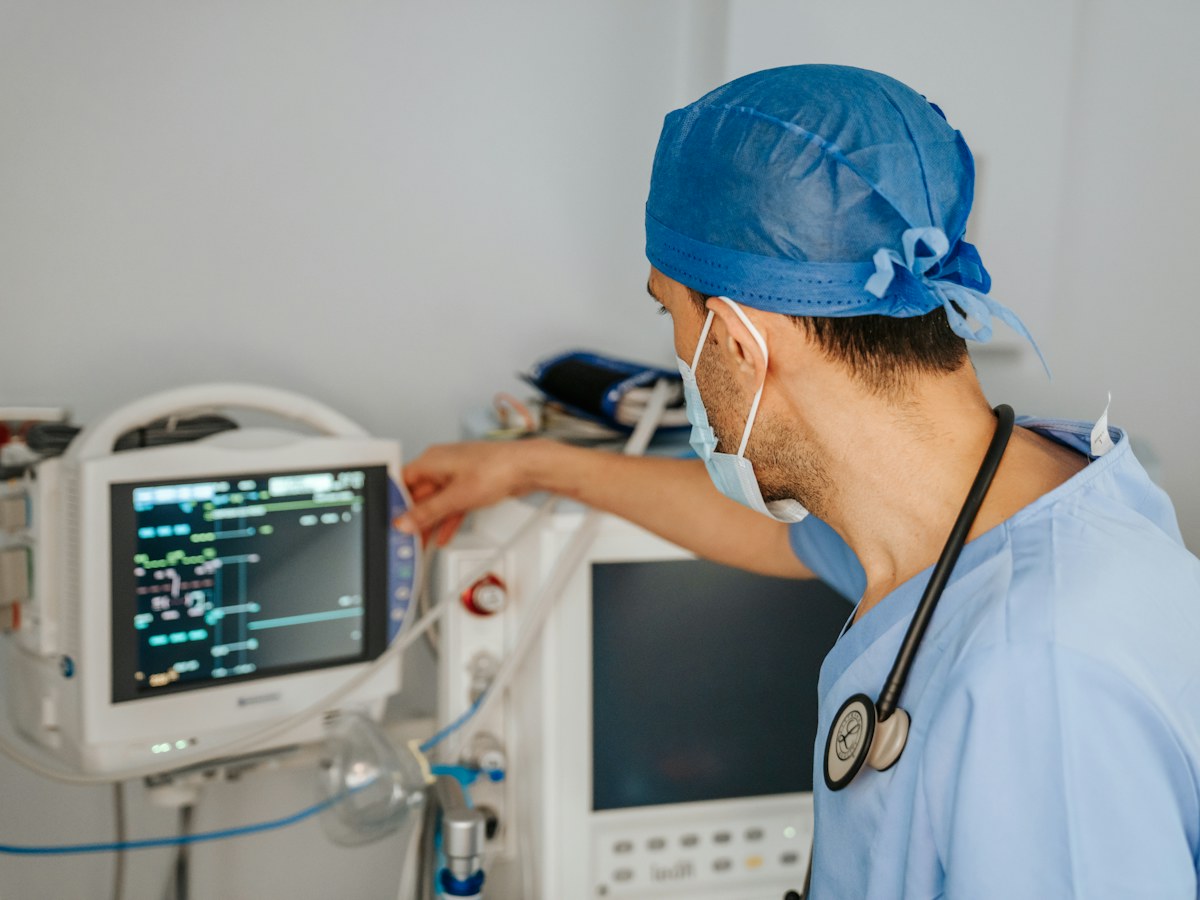 Clinician in scrubs with a stethoscope reviewing a patient monitor