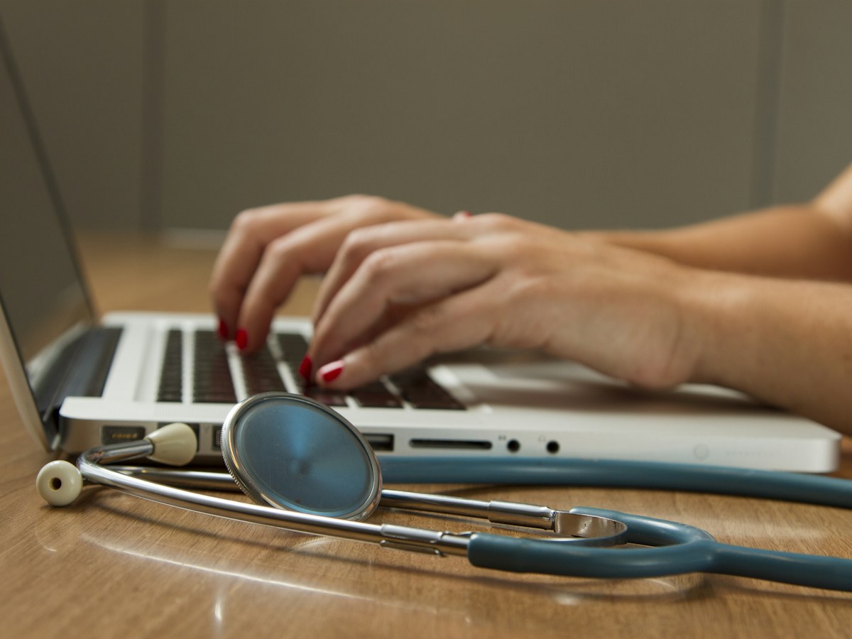 Healthcare professional working on a laptop with a stethoscope on the desk